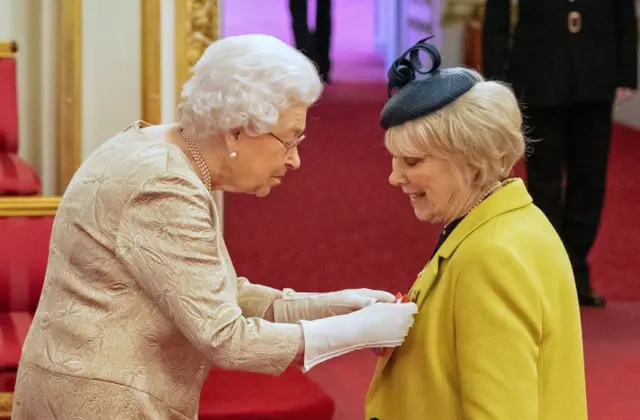 Queen Elizabeth II wears gloves as she awards a CBE to Miss Anne Craig