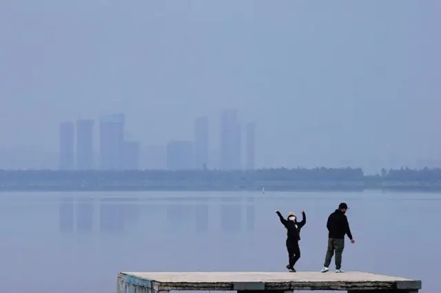 A woman wearing a face mask dances on the East Lake in Wuhan, Hubei province,