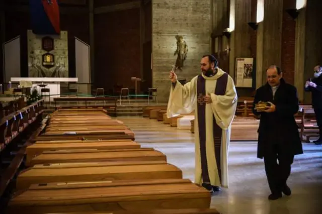 A priest blesses coffins of people who died with Covid-19 in northern Italy