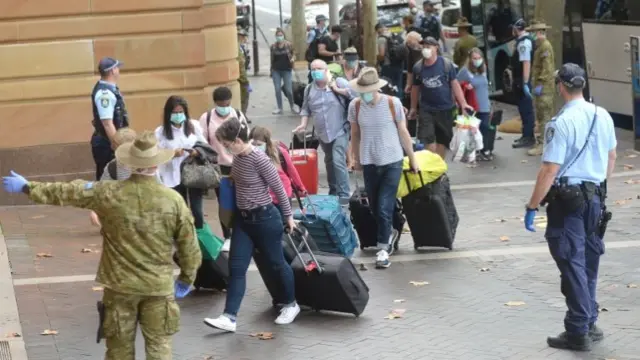 Police and military officer guide returned travellers to their hotel isolation rooms in Sydney