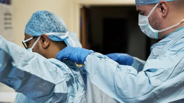 Shot of two surgeons helping each other get dressed in preparation for a surgery