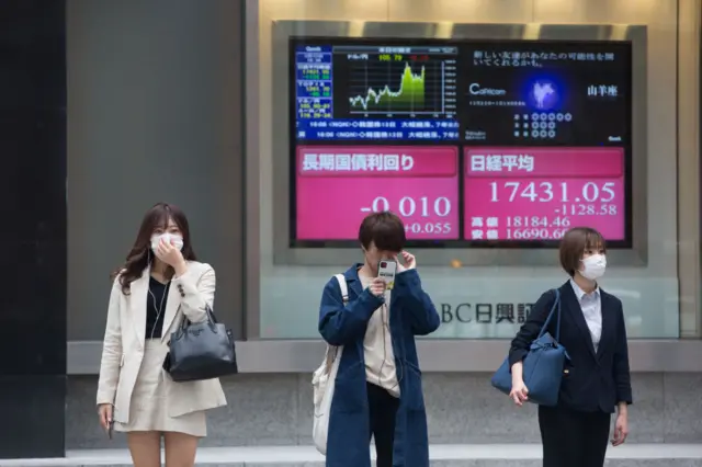 Pedestrians wait to cross the street in Tokyo in front of an electronic board showing the Nikkei 225 index