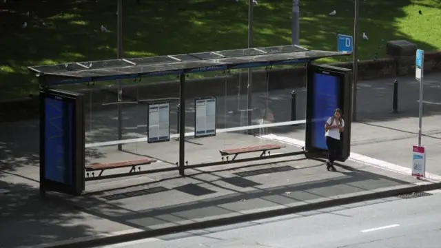 Woman waits by empty bus shelter in Sydney city