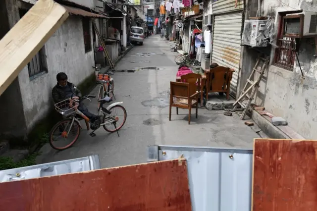 People rest outside houses that are behind barriers blocking the alley in Wuhan. Photo: 4 March 2020