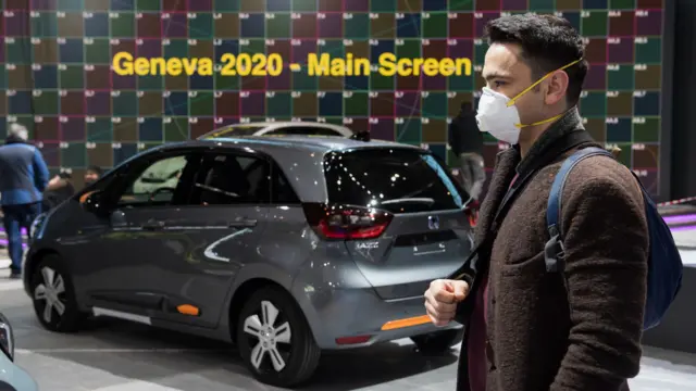 A man wearing a mask stands near a car on at the Geneva International Motor Show, which has been cancelled due to the Covid-19 epidemic