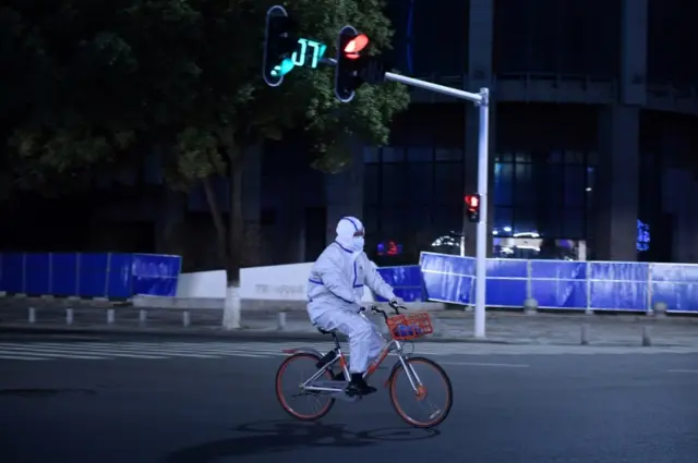 A man in a protective suit rides a bicycle in Wuhan. Photo: 4 March 2020