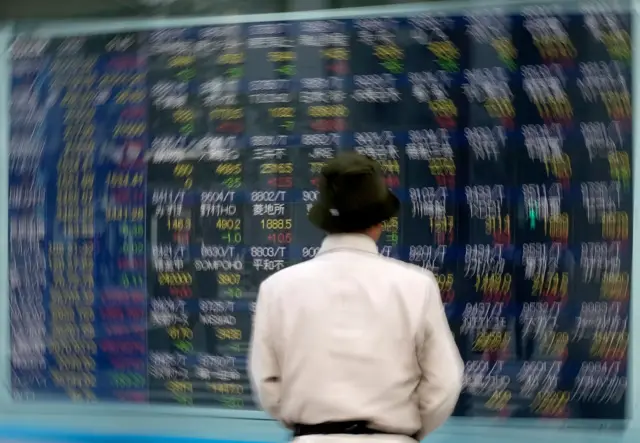 A pedestrian looks at an electronic quotation board displaying stock prices for Japanese companies on the Tokyo Stock Exchange.