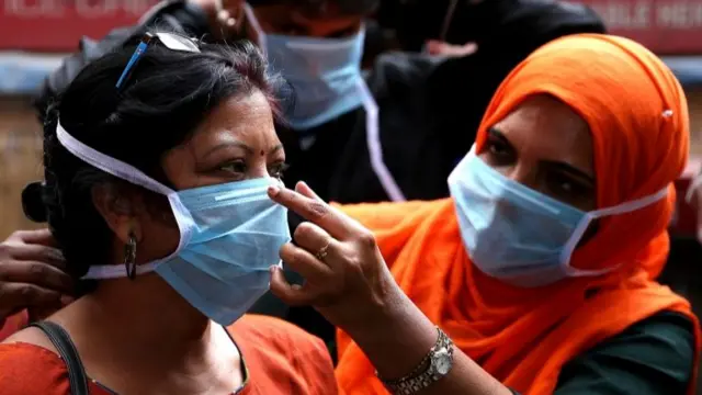 Women wearing medical masks in Bangalore, a medic helps a woman fit her mask