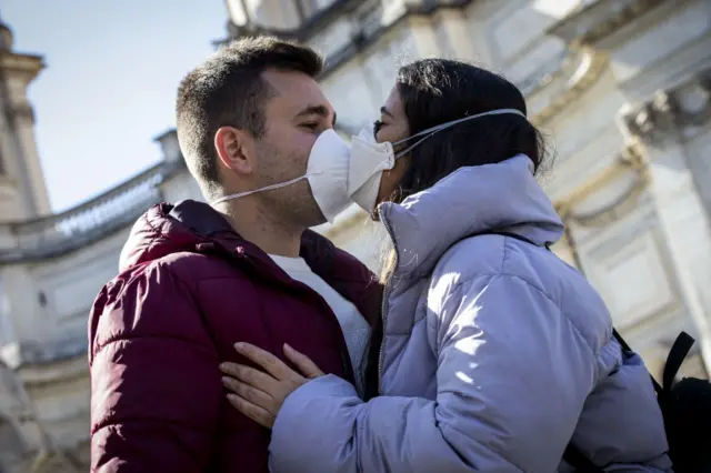 Two young people wearing protective face masks kiss in central Rome, Italy, on 4 March 2020