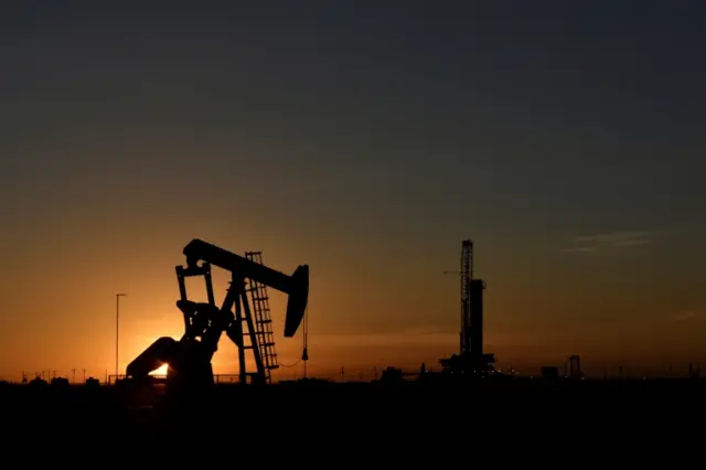 A pump jack operates in front of a drilling rig at sunset in an oil field in Texas, the US. File photo