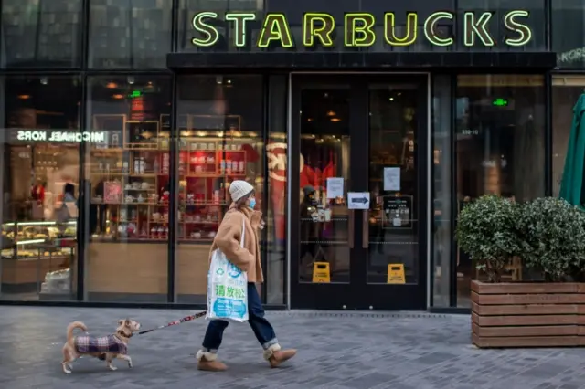 A woman walks past a Starbucks coffee shop walks her dog in Beijing on January 30, 2020