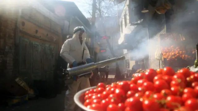 A firefighters wearing protective suits spray disinfect at a market in Tehran