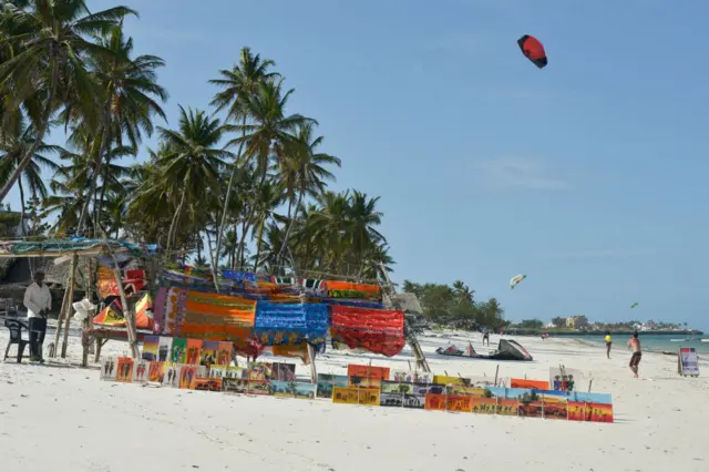 A vendor displays his goods while a tourist flies a kite on the beach near Mombasa, Kenya