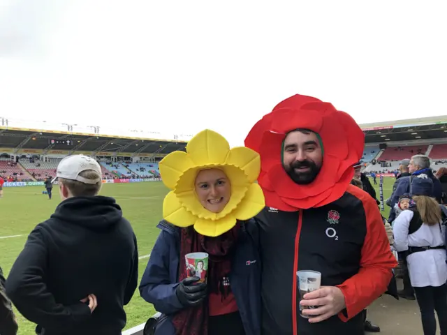 A couple with the woman wearing a daffodil hat and the man wearing a rose hat