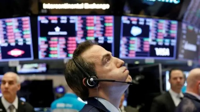 A trader wearing a headset looks exasperated