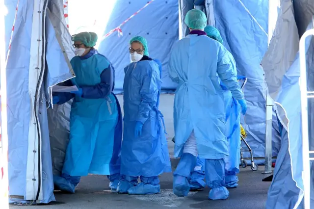 Italian healthcare staff of the infectious diseases department at Padova Hospital wear protective suits and masks as they swab people waiting in line in front of a civil protection tent. Photo: 6 March 2020