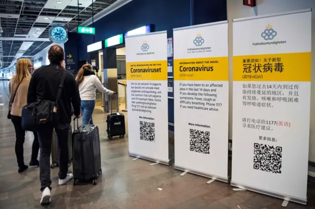 Passengers in Stockholm"s Arlanda airport walk past coronavirus warning signs in different languages