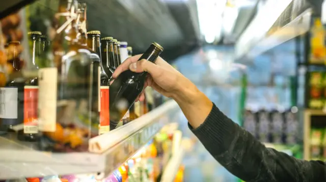 A man takes a bottle of a shelf in a shop