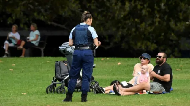 Police officer asks a family sitting in the park to leave because of new laws