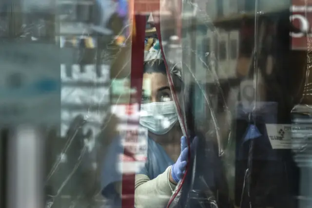 A pharmacist in in the Bronx works behind a plastic curtain