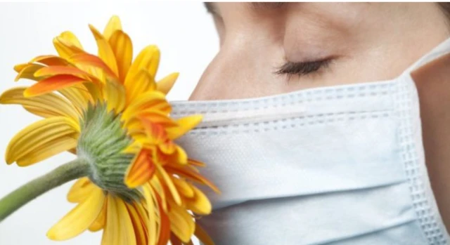 Woman smelling flower while wearing face mask