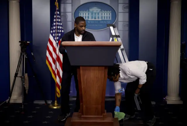 Cleaners wipe down the White House podium before the briefing