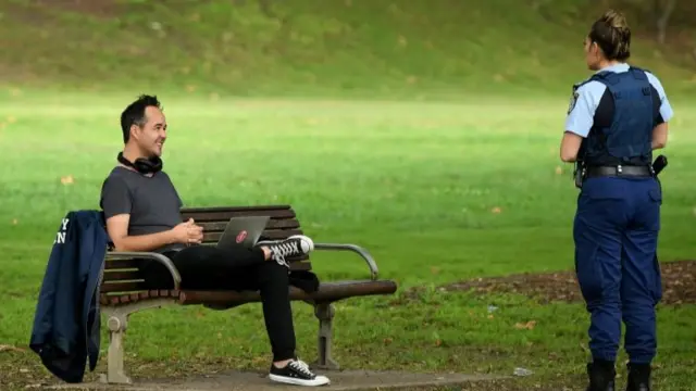 Police officer asks a man sitting on a park bench to leave