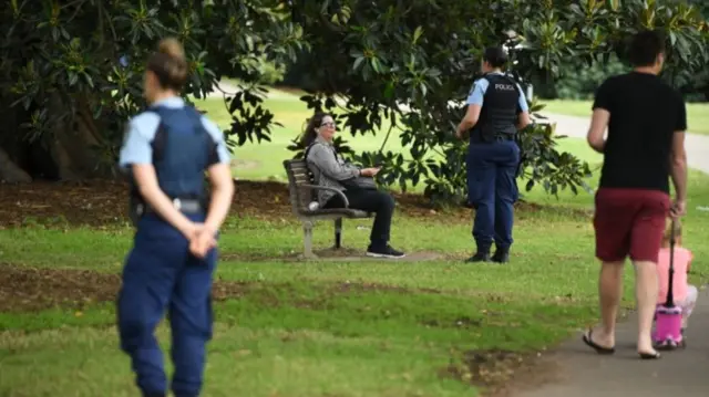 Police officers ask a woman sitting on a bench in a Sydney park to leave