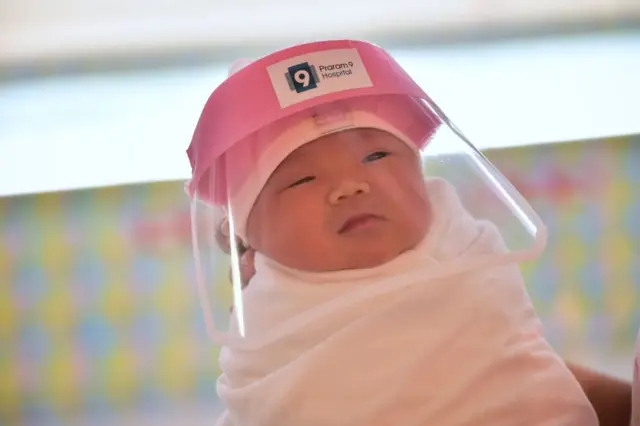 This photo taken through a glass window at a maternity ward shows a newborn baby wearing a face shield