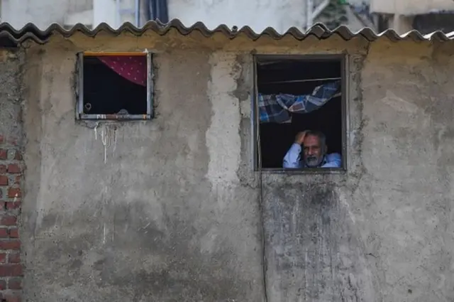 An Indian man looks out of the window at his home