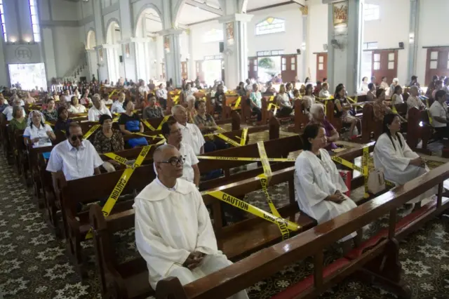 Catholic faithfuls sit on chairs with yellow line tapes