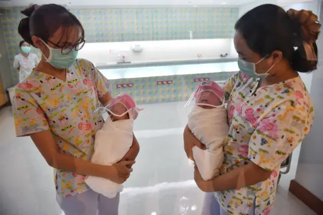 This photo taken through a glass window at a maternity ward shows nurses holding newborn babies wearing face shields