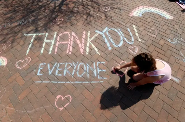 A girl writes 'thank you' on a pavement in Broadway, Britain