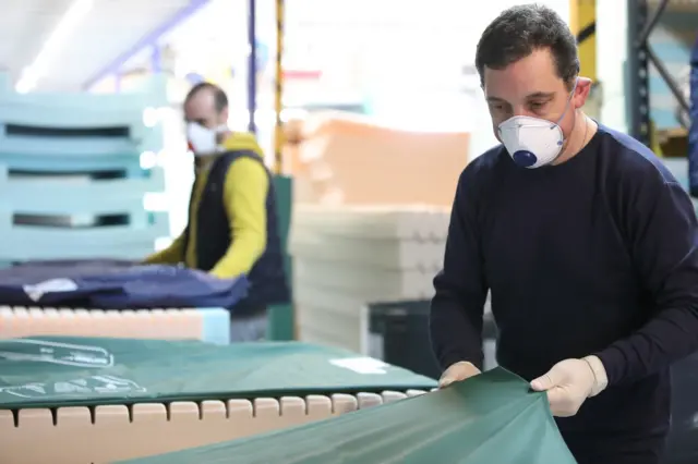 Man wearing a mask pulling a sheet over a mattress