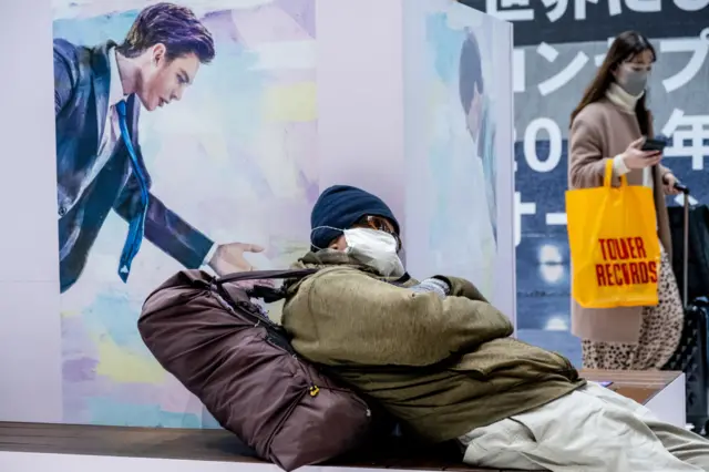 A homeless man wearing a mask sleeps on a bench in Japan