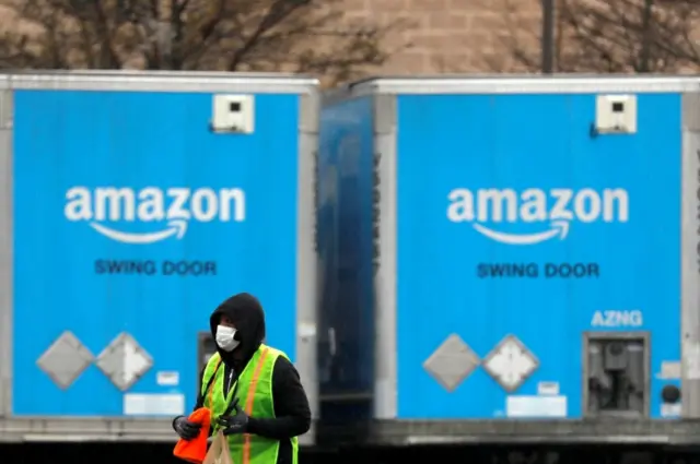 A worker in a face mask walks by trucks parked at an Amazon facility in Long Island, New York