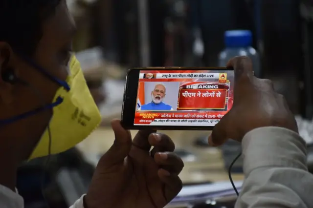 A man wearing a facemask as a preventive measure against COVID-19 coronovirus listens Prime Minister Narendra Modi's address to the nation on his mobile phone in Jabalpur on March, 19, 2020.