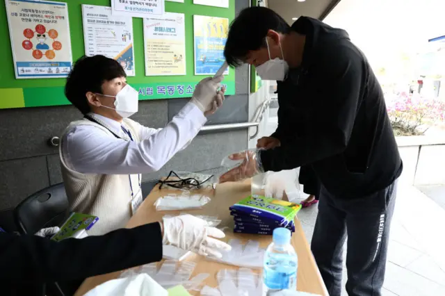 A South Korean man wears plastic gloves has his temperature checked upon his arrival to cast his vote for Parliamentary election