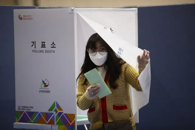 A South Korean woman wears a mask and plastic gloves cast her vote