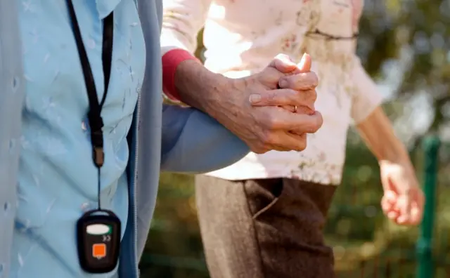 A resident holds the hand of a member of staff at a UK care home