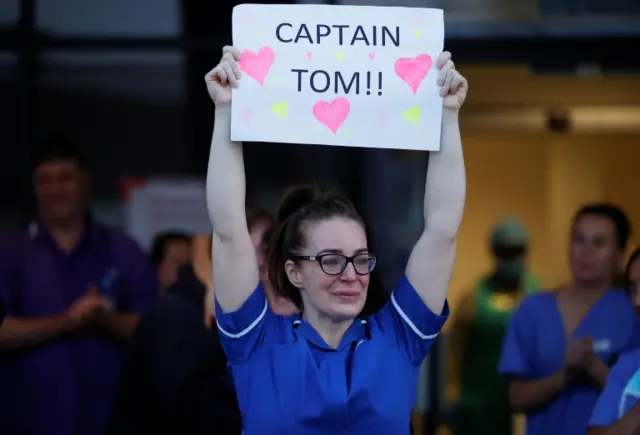 An NHS worker holds a sign with a message to Captain Tom