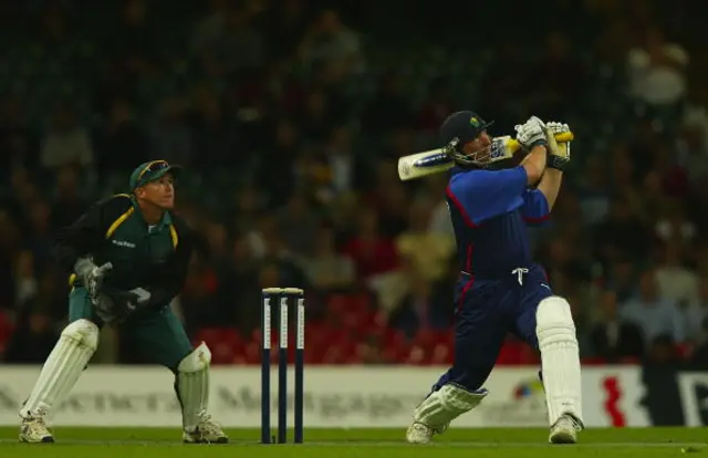 Rest of the World's Andy Flower (left) watches on as Matthew Maynard hits out for Britain in their 2002 Power Cricket match