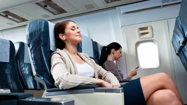 Two women relax on a plane with a free seat between them