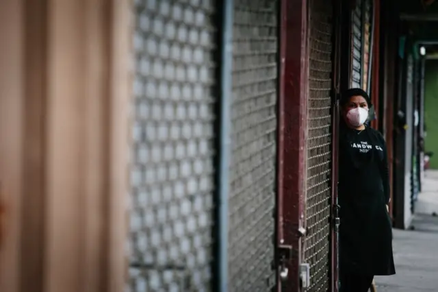 A woman wears a face mask while waiting for customers at a sandwich shop in Brooklyn, New York