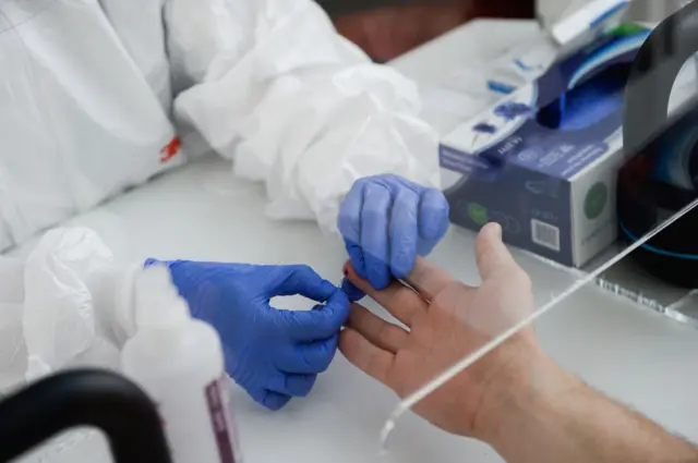 A health worker wearing PPE extracts blood from a patient to make an antibody test for Covid-19