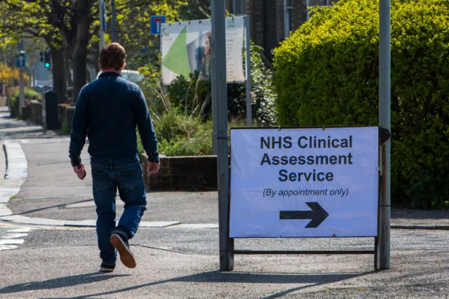 A man walks past a sign for an NHS Clinical Assessment Service