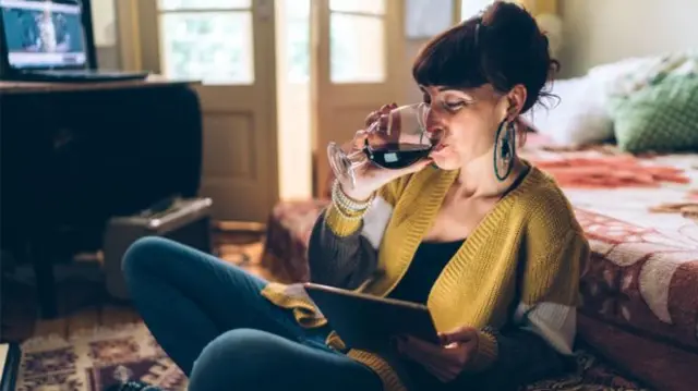 A woman drinks a glass of wine in a stock image