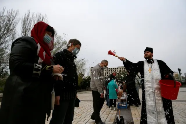 A priest sprinkles holy water on believers and their "paskha" cakes, eggs and other food during the Orthodox Easter celebrations amid the coronavirus disease outbreak in the rebel-controlled city of Donetsk, Ukraine April 19 2020