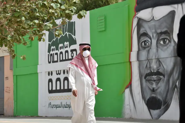 Man wearing a mask walks past mural of King Salman bin Abdulaziz in Riyadh (file photo)