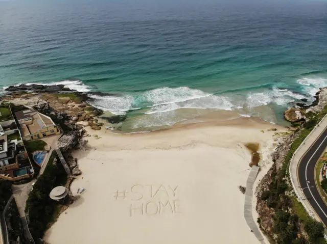 An aerial view of a notice dug into the sand reading #STAYHOME on Tamarama Beach